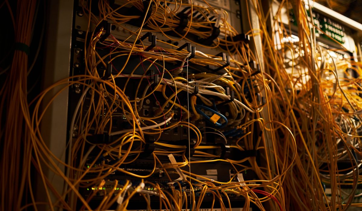 Close-up of a server rack situated in a data center filled with tangled cables and various network equipment illuminating low light environment